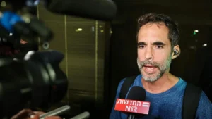 A man is being interviewed by a news reporter, with a microphone from "N12" visible in the foreground.