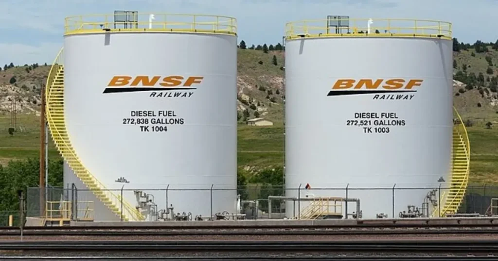 The image shows two large BNSF Railway diesel fuel storage tanks, each containing a significant volume of diesel fuel, situated near a railway track in a rural setting.
