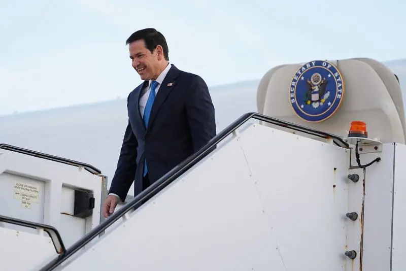 The image shows a man in a suit descending a staircase from an aircraft with the U.S. Secretary of State seal visible on the side.