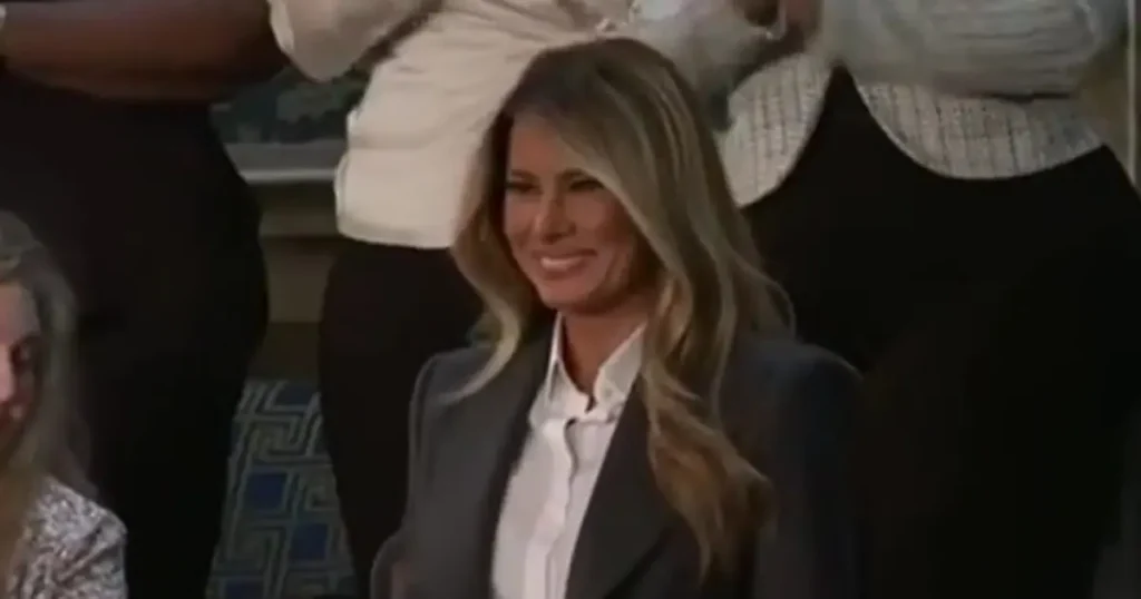 The image shows a woman in a professional setting, smiling and wearing a dark blazer over a white shirt.