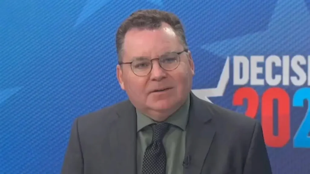 The image shows a man in a suit and tie speaking in front of a blue background with the text "DECISIVE 2021."