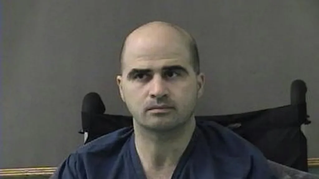 The image shows a person in a dark-colored shirt seated in a chair, with a plain background.