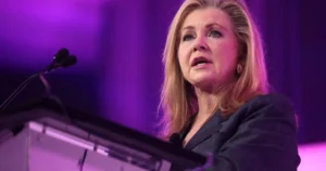 A woman is speaking at a podium in front of a purple-lit background.