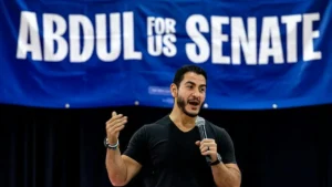 A man is speaking into a microphone in front of a banner that reads "ABDUL FOR US SENATE."