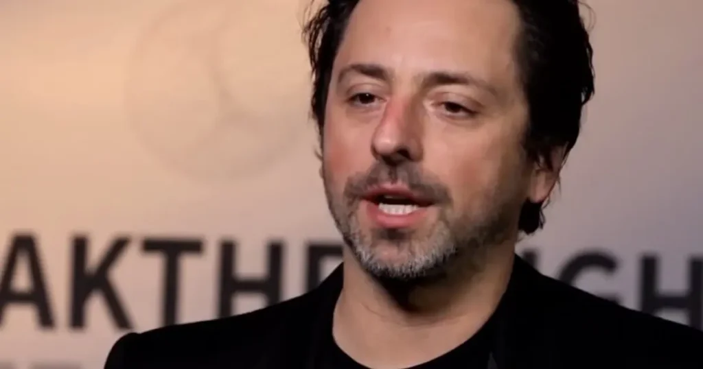 The image shows a man speaking at an event with a backdrop that includes the text "BREAK THE."