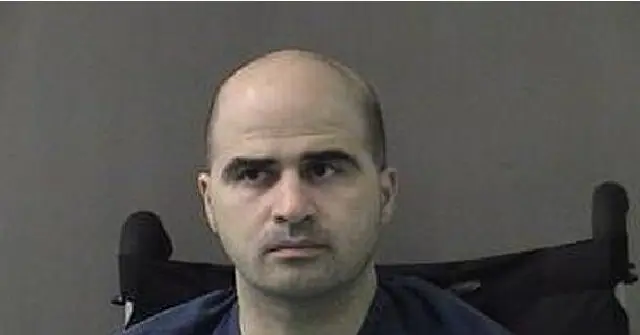 The image appears to be a mugshot of a man seated in a wheelchair, wearing a dark-colored shirt.