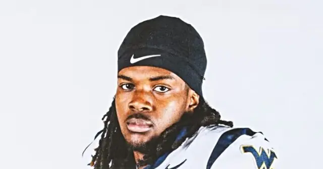 The image shows a person wearing a black Nike beanie and a white jersey with a blue "W" logo, set against a plain background.
