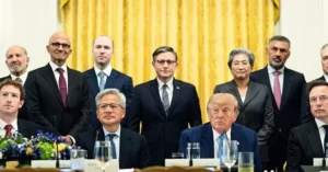 The image shows a formal meeting with a group of individuals in suits, seated and standing, in what appears to be a government or official setting.