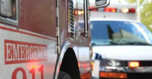 The image shows an emergency vehicle with the word "EMERGENCY" and the number "011" prominently displayed on its side, indicating it is part of a response team.