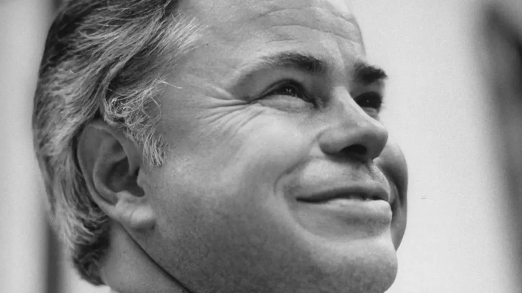The black-and-white news photo captures a close-up of a man with a thoughtful expression, gazing upwards.