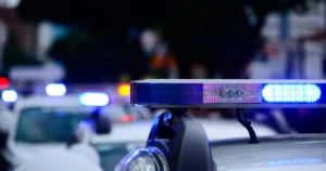 A police car with flashing blue lights is shown in the foreground, with other emergency vehicles in the background.