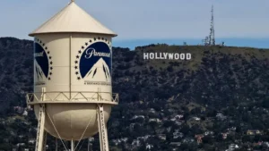A water tower with the Paramount logo stands prominently in the foreground, with the iconic Hollywood sign visible in the background.