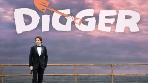 A man in a tuxedo stands in front of a backdrop featuring the word "DIGGER" with a graphic of a shovel.