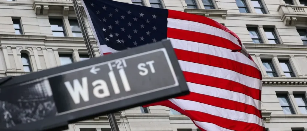 The image shows a Wall Street street sign in front of an American flag, symbolizing the financial district of New York City.
