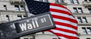 The image shows a Wall Street street sign in front of an American flag, symbolizing the financial district of New York City.