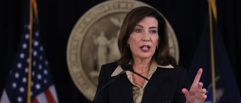A woman is speaking at a podium with an American flag and a seal in the background.