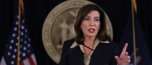 A woman is speaking at a podium with an American flag and a seal in the background.