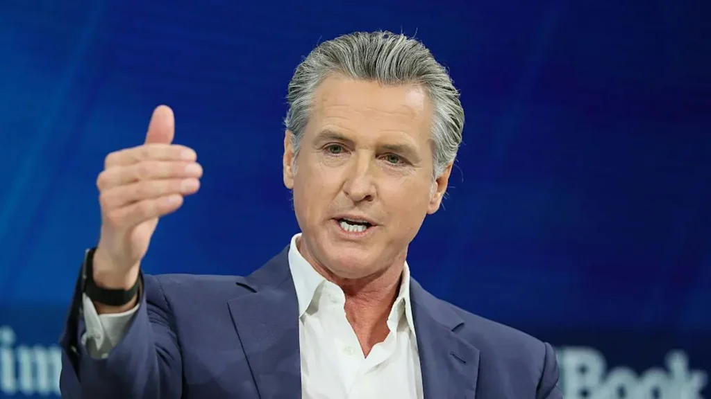 The image shows a man in a suit gesturing with his right hand, likely during a speech or presentation.