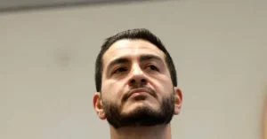 The image shows a close-up of a man with a beard and short dark hair, looking upwards.