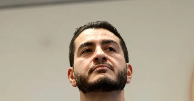 The image shows a close-up of a man with a beard and short dark hair, looking upwards.