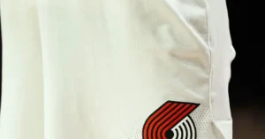 The image shows a close-up of a white sports jersey with a red and black logo on the lower right side.