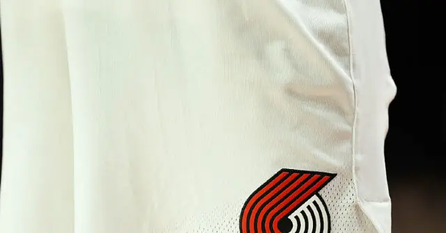 The image shows a close-up of a white sports jersey with a red and black logo on the lower right side.