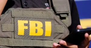 The image shows a person wearing an FBI vest while holding a smartphone.