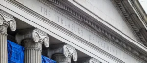 The image shows the facade of the Treasury Department building, featuring classical columns and inscriptions.