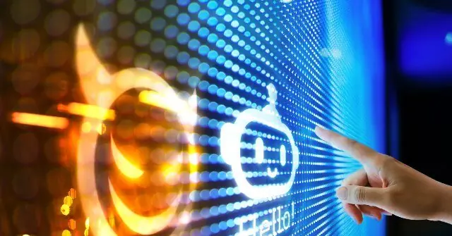 A hand interacts with a futuristic interface displaying a smiling robot icon and the word "Hello!" on a vibrant LED screen.