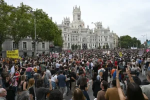 A large crowd gathers in front of a grand building, holding signs and participating in a protest.