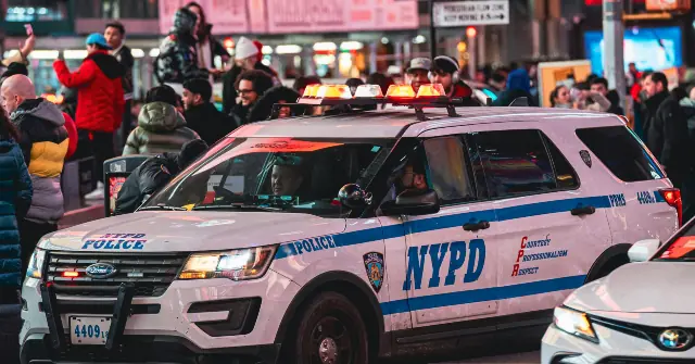 An NYPD police vehicle is parked in a busy urban area with people around, likely during a public event or gathering.