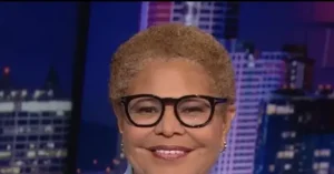The image shows a person wearing glasses and smiling, with a cityscape in the background.