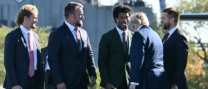 A group of men in suits and ties are seen interacting outdoors, with one man smiling and engaging in conversation with another.
