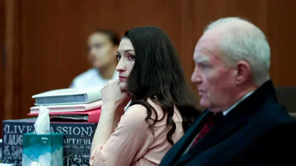 The image shows two individuals seated in what appears to be a courtroom setting, with one person appearing contemplative and the other looking forward.