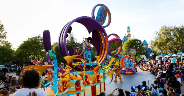 A vibrant parade float featuring colorful, whimsical designs and performers is showcased in front of a crowd at a theme park.