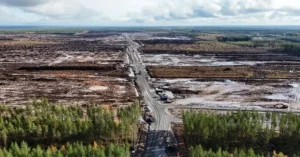 The image shows an aerial view of a large area of land that appears to have been affected by a fire, with charred ground and a road cutting through the devastated landscape.