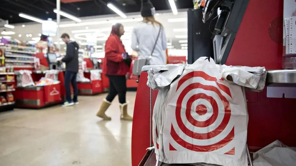 A Target shopping bag is seen on a checkout counter in a store, with customers in the background.