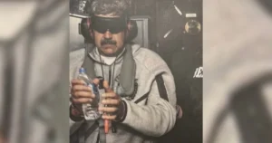 The image shows a person wearing ear protection and holding a water bottle and a small object, possibly in a shooting range or similar environment.