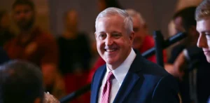 A man in a suit and tie smiles at the camera in a crowded setting.