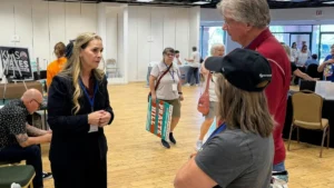 A woman in a black suit is engaged in conversation with a man in a red shirt at what appears to be a political event or campaign gathering.