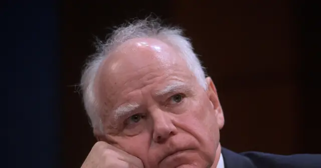 The image shows a close-up of a person with white hair, wearing a suit, appearing to be in a serious or contemplative mood.