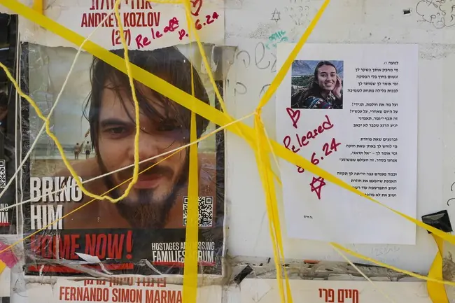 The image shows posters with messages and photos, including one with the text "BRING HIM HOME NOW!" and another with a release date, tied with yellow ribbons.