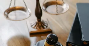 The image depicts a symbolic representation of justice, featuring a gavel, a book, and a scale, suggesting themes of law and legal proceedings.