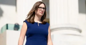 A woman in a blue dress walks in front of a white building with columns.