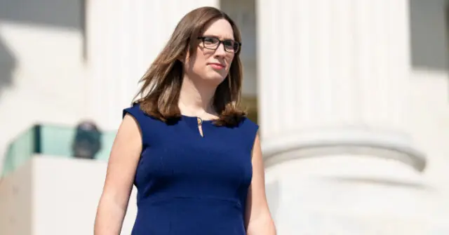 A woman in a blue dress walks in front of a white building with columns.
