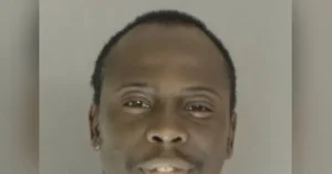 The image appears to be a mugshot of a man with short hair and a mustache, taken against a plain background.