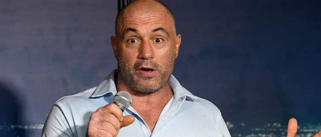 The image shows a man speaking into a microphone, appearing engaged and expressive.