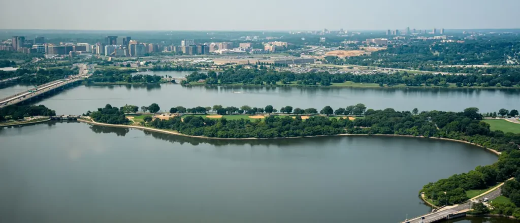 The image shows an aerial view of a cityscape with a large body of water in the foreground, surrounded by greenery and urban infrastructure.