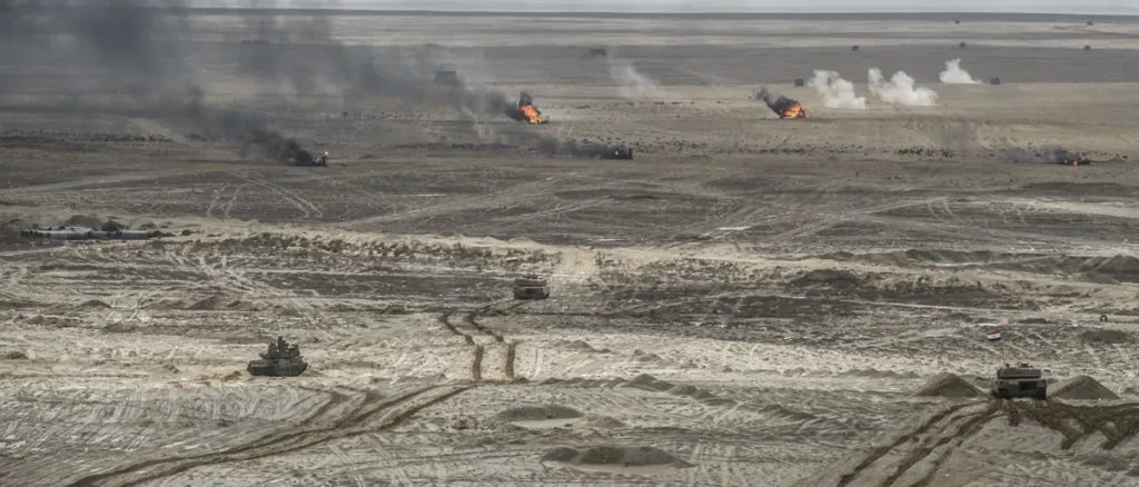 The image depicts a desert battlefield with military vehicles and smoke rising from explosions in the distance.