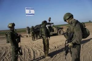 The image shows a group of soldiers standing in a desert area with an Israeli flag in the background, indicating a military operation or deployment.